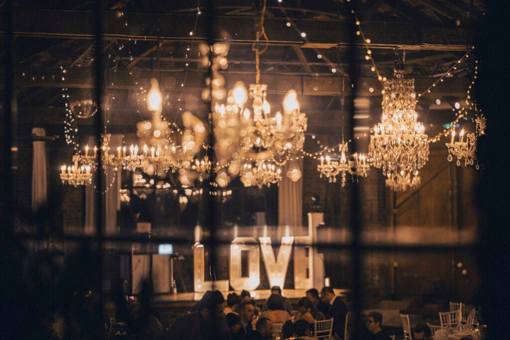 Stimmungsvolle Hochzeitsfeier mit Kronleuchtern und LOVE-Leuchtschrift in urbaner Halle